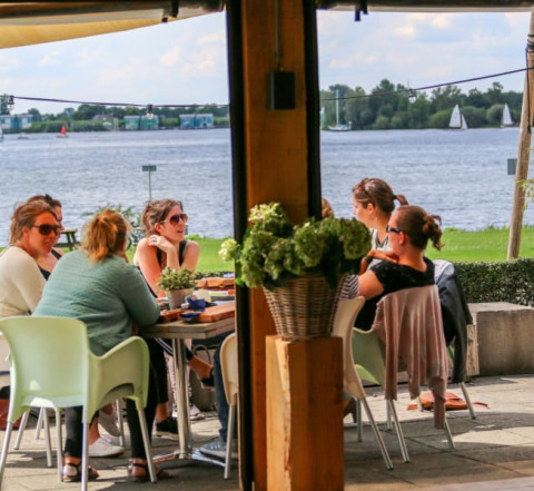 Gruppe von Menschen sitzt an einem Tisch im Safari-Zelt am Wasser im Recreatiepark Riverside, Niederlande.