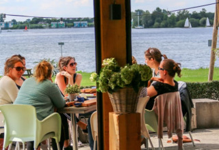 Gruppo di persone sedute a un tavolo sotto una tenda safari vicino all’acqua al Recreatiepark Riverside, Paesi Bassi.