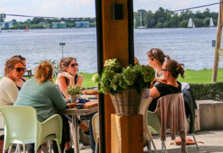 Groupe de personnes assises à une table sous une tente safari près de l’eau au Recreatiepark Riverside, Pays-Bas.
