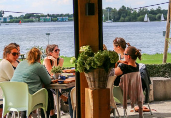 Gruppo di persone sedute a un tavolo sotto una tenda safari vicino all’acqua al Recreatiepark Riverside, Paesi Bassi.
