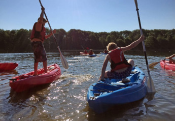 Børn i redningsveste leger og padler i kajakker på en sø ved Recreatiepark Riverside i Holland.