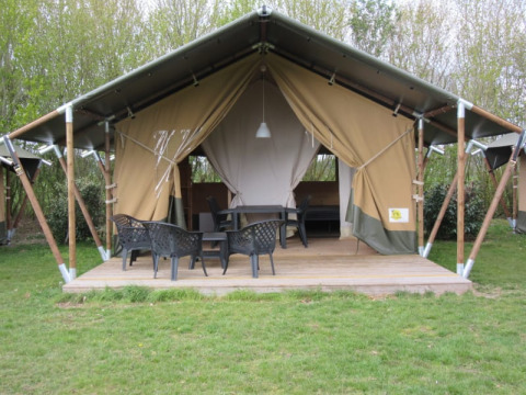 Safaritent met houten terras en zwarte stoelen, omgeven door bomen en een groene grasmat.