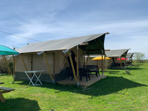 Safari-Zelte auf dem Minicamping Sous les Cloches in Frankreich mit bunten Sonnenschirmen und Rasen.