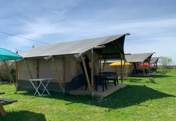 Safari-telte på Minicamping Sous les Cloches i Frankrig med farverige parasoller og grøn græsplæne.