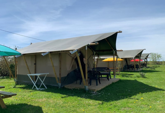 Safari tents at Minicamping Sous les Cloches in France with colorful umbrellas and green grass lawn.