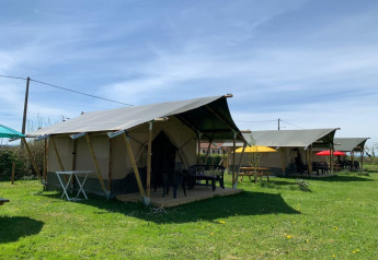 Safari tents at Minicamping Sous les Cloches in France with outdoor seating on a green grassy area.