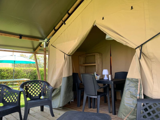 Safari tent with plastic chairs and table at Minicamping Sous les Cloches campsite in France.