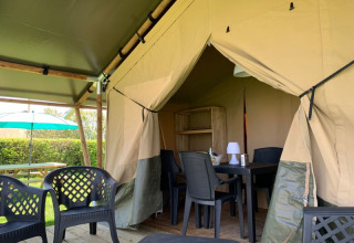 Safari tent with plastic chairs and table at Minicamping Sous les Cloches campsite in France.