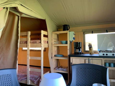 Innenaufnahme eines Safarizelts bei Minicamping Sous les Cloches, mit Küche und Etagenbett in Frankreich.
