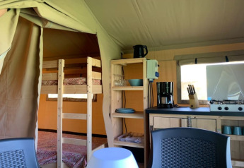 Interno di una tenda safari presso Minicamping Sous les Cloches, Francia, con cucina e letti a castello.