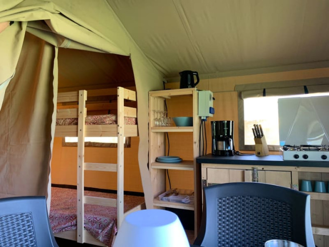 Binnenkant van een safaritent op Minicamping Sous les Cloches, Frankrijk, met keuken en stapelbedden.