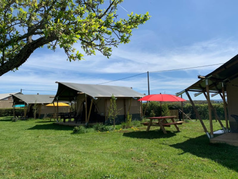 Tenda safari al Minicamping Sous les Cloches in Francia, prato verde, tavolo da picnic e ombrellone rosso.