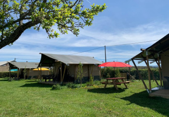 Tenda safari al Minicamping Sous les Cloches in Francia, prato verde, tavolo da picnic e ombrellone rosso.