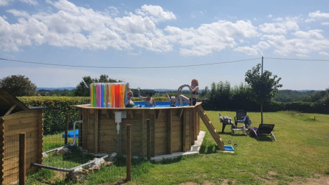 Aufnahme eines erhöhten Pools mit Menschen im Wasser auf einem grünen Campingplatz bei Safari tent am Minicamping Sous les Cloches, Frankreich.