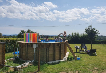 Aufnahme eines erhöhten Pools mit Menschen im Wasser auf einem grünen Campingplatz bei Safari tent am Minicamping Sous les Cloches, Frankreich.