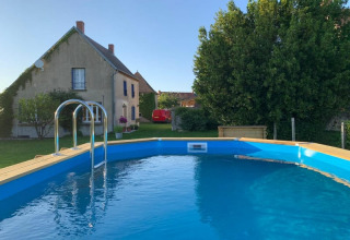 Udendørs swimmingpool foran et landligt hus og grønne træer på Safari tent at Minicamping Sous les Cloches, Frankrig.