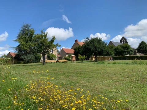 Open green field with wildflowers, trees and buildings in the background at Safari tent, Minicamping Sous les Cloches, France.