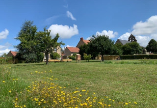 Open green field with wildflowers, trees and buildings in the background at Safari tent, Minicamping Sous les Cloches, France.