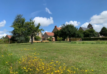 Open green field with wildflowers, trees and buildings in the background at Safari tent, Minicamping Sous les Cloches, France.