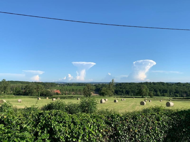 Uitzicht op hooibalen in een groen veld met paddenstoelvormige wolken bij Safari tent op Minicamping Sous les Cloches.