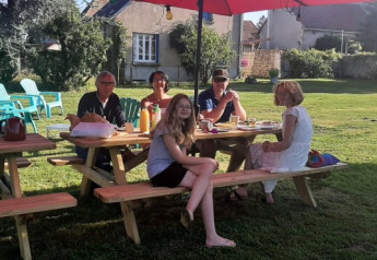 Fünf Personen sitzen an einem Picknicktisch unter einem roten Sonnenschirm auf Safari tent at Minicamping Sous les Cloches in Frankreich.
