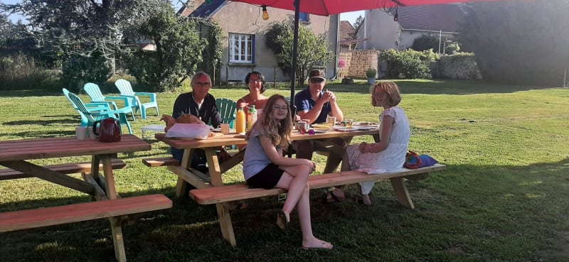 Fünf Personen sitzen an einem Picknicktisch unter einem roten Sonnenschirm auf Safari tent at Minicamping Sous les Cloches in Frankreich.