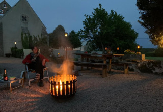 Person sitting by a fire pit in front of the safari tent at Minicamping Sous les Cloches in France at dusk.