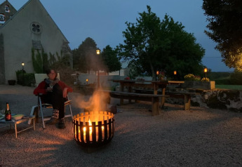 Iemand zit bij een vuurkorf voor de safaritent op Minicamping Sous les Cloches in Frankrijk in de avond.