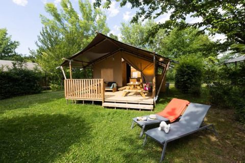 Tienda safari con instalaciones sanitarias, terraza de madera, mesa de picnic y tumbonas en jardín soleado.