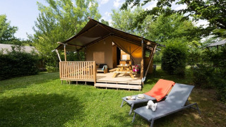 Tienda safari con instalaciones sanitarias, terraza de madera, mesa de picnic y tumbonas en jardín soleado.