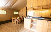 Interieur van een gezellige safaritent met houten meubels en kitchenette bij Le Camp de Florence, Frankrijk.