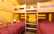 Interieur van Safari tent + sanitair bij Le Camp de Florence, Frankrijk, met stapelbed en kinderspeelgoed.