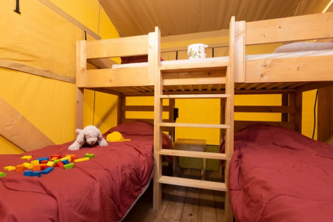 Intérieur d'une tente Safari + sanitaire au Camp de Florence, France, avec lits superposés et jouets d'enfant.