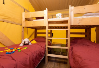 Interior de tienda Safari + sanitario en Le Camp de Florence, Francia, con literas y juguetes infantiles.