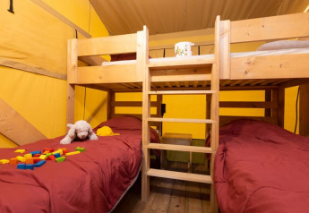 Interior de tienda Safari + sanitario en Le Camp de Florence, Francia, con literas y juguetes infantiles.