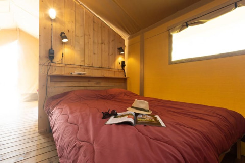 Indretning af soveværelse i et safari-telt med træpaneler på Le Camp de Florence, Frankrig, med dobbeltseng.