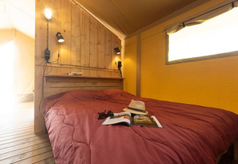Chambre d’une tente safari avec mur en bois et lit double au Camp de Florence, France, bien éclairée.