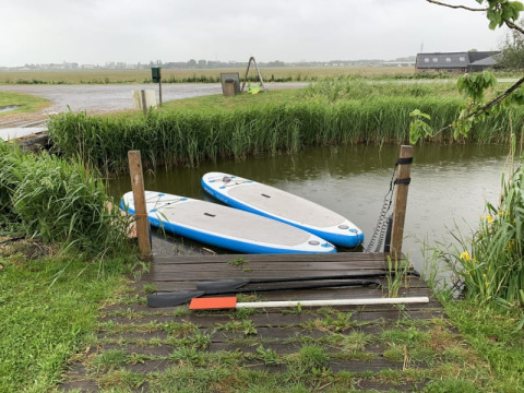To paddleboards ved en lille træbro, omgivet af grønt græs og siv på Boerencamping Swarthoeve, Holland.