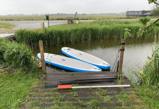 Zwei Paddleboards liegen an einem kleinen Steg an einem Wasserkanal bei Boerencamping Swarthoeve, Niederlande.