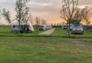 Wohnwagen und Wohnmobile stehen auf einer Wiese beim Sonnenuntergang auf dem Bauernhofcamping Swarthoeve.