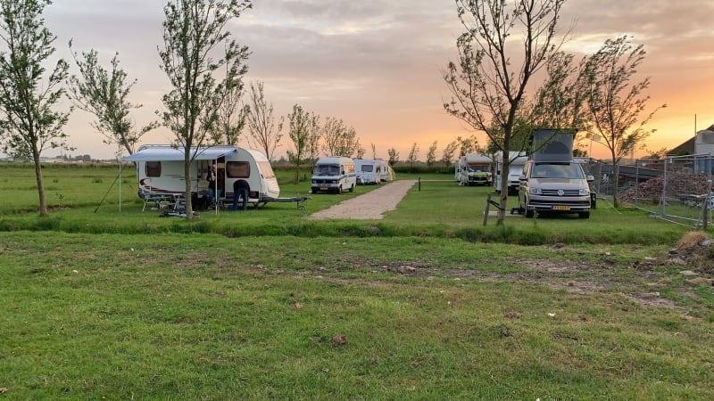 Caravans en campers geparkeerd op een groen grasveld bij zonsondergang op Boerencamping Swarthoeve.
