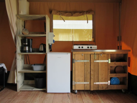 Cocina interior de una tienda safari en Boerencamping Swarthoeve, Países Bajos, con estantes y estufa.