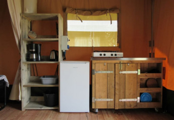 Cocina interior de una tienda safari en Boerencamping Swarthoeve, Países Bajos, con estantes y estufa.