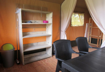 Interior photo of a safari tent at Boerencamping Swarthoeve, with plastic chairs and wooden shelf, Netherlands.