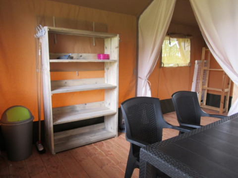 Interior photo of a safari tent at Boerencamping Swarthoeve, with plastic chairs and wooden shelf, Netherlands.