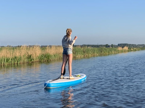 En person står på et paddleboard på roligt vand ved Safari tent på Boerencamping Swarthoeve, Holland.