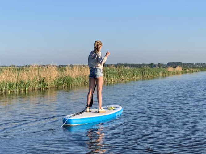 Eine Person steht auf einem Paddleboard auf ruhigem Wasser nahe Safari tent bei Boerencamping Swarthoeve, Niederlande.