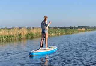 Eine Person steht auf einem Paddleboard auf ruhigem Wasser nahe Safari tent bei Boerencamping Swarthoeve, Niederlande.
