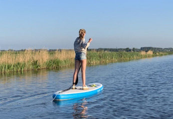 En person står på et paddleboard på roligt vand ved Safari tent på Boerencamping Swarthoeve, Holland.
