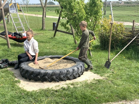 Kinder spielen in einem Sandkasten aus einem großen Reifen bei Safari Tent auf Boerencamping Swarthoeve, Niederlande.